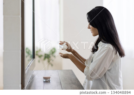 A woman applying lotion in front of a mirror A woman applying lotion in front of a mirror 134048894