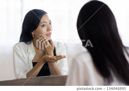 A woman applying lotion in front of a mirror 134048895
