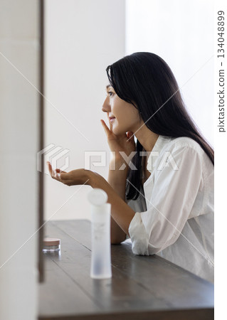 A woman applying lotion in front of a mirror 134048899