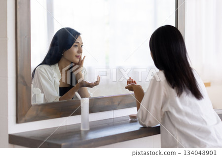 A woman applying lotion in front of a mirror 134048901