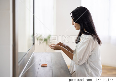 A woman applying makeup with a powder puff in front of a mirror 134049177