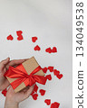 Person Holds Gift Box With Red Ribbon And Hearts For Valentine's Day 134049538