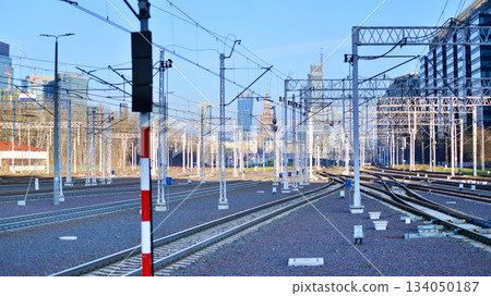 Tracks and electric high voltage for electric trains wires on reinforced concrete and metal masts against the backdrop of a city skyscrapers on a winter day. 134050187