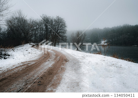 Lonely Dirt Road Curving Along a Snowy Riverbank in Winter Fog Lonely Dirt Road Curving Along a Snowy Riverbank in Winter Fog 134050411