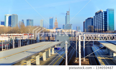 Tracks and electric high voltage for electric trains wires on reinforced concrete and metal masts against the backdrop of a railway station and city skyscrapers on a winter day. 134050487