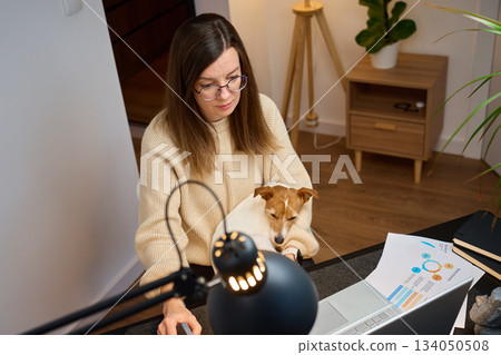 Woman working on laptop at home with dog on her lap 134050508