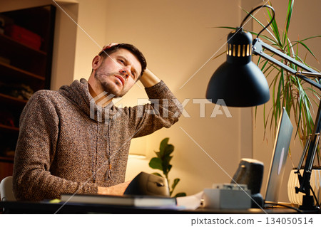 Man stretching neck while working at desk in home office Man stretching neck while working at desk in home office 134050514