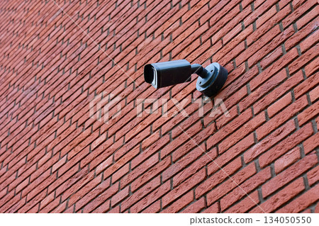 Surveillance camera mounted on a red brick wall exterior 134050550