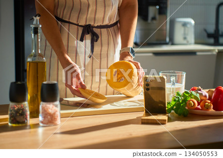 Woman slicing pumpkin on cutting board in kitchen Woman slicing pumpkin on cutting board in kitchen 134050553