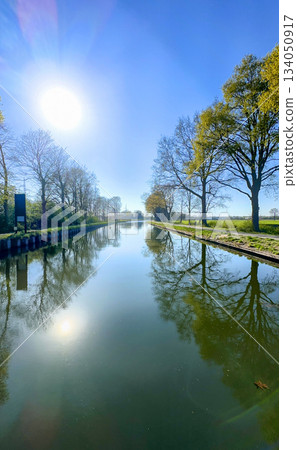 Serene Reflections by the Glistening Canal Beneath a Bright and Warm Sunlight on a Beautiful Day Serene Reflections by the Glistening Canal Beneath a Bright and Warm Sunlight on a Beautiful Day 134050917