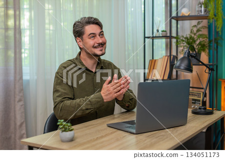 Middle-aged man pleased clasping hands reviewing laptop report celebrates big deal closure at table 134051173