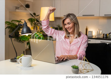 Adult woman receives bonus notification on laptop smiles celebrates raises hand excited jackpot win 134051176