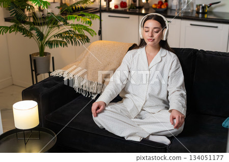 Young woman listens to rain in headphones meditates slow breath calm mind quiet rest evening still Young woman listens to rain in headphones meditates slow breath calm mind quiet rest evening still 134051177