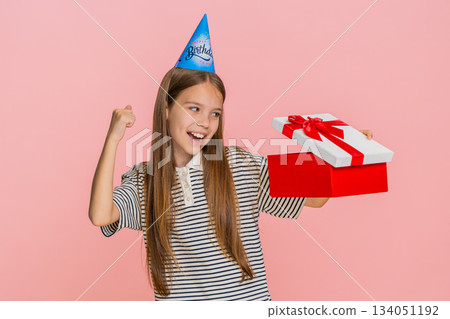 Child girl jumps with joy waves hands celebrating birthday while happily receiving surprise gift box 134051192