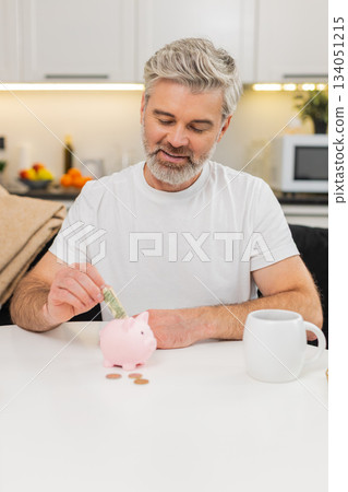 Middle-aged man puts money cash coins in piggy bank saving budget promise savings dollar discipline Middle-aged man puts money cash coins in piggy bank saving budget promise savings dollar discipline 134051215