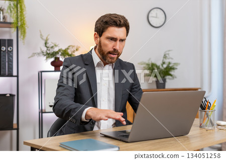 Middle-aged businessman sees laptop freeze eyes widen press key reboots system upset data loss after 134051258