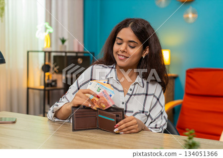 Indian rich woman counting euro cash placing bills into wallet feeling satisfied, proud wealth calm Indian rich woman counting euro cash placing bills into wallet feeling satisfied, proud wealth calm 134051366