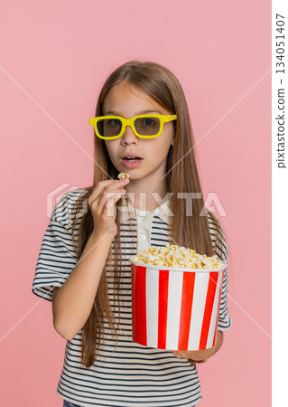 Child girl kid happily eating popcorn while watching funny cartoon laughing and smiling cheerfully 134051407