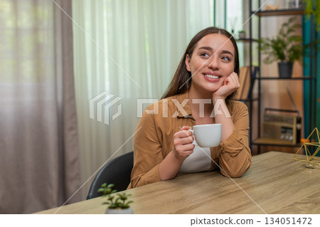 Young woman holding coffee cup thinking peacefully with happy calm mood during quiet break morning 134051472