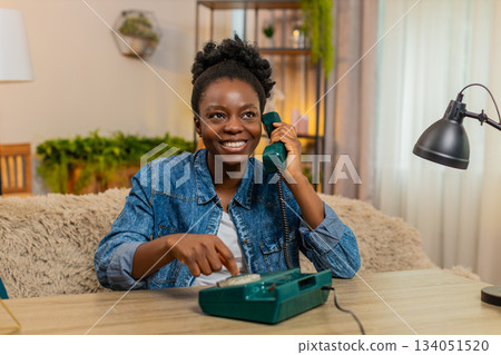 African American young woman using vintage wired telephone with curiosity while sitting at home African American young woman using vintage wired telephone with curiosity while sitting at home 134051520