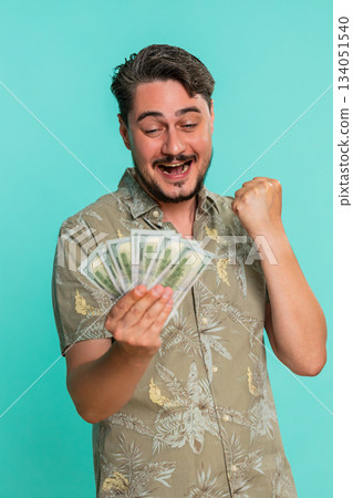 Man holding raising dollars cash money in excitement smiling celebrating financial win achievement Man holding raising dollars cash money in excitement smiling celebrating financial win achievement 134051540