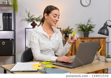 Young businesswoman opens laptop lays stickers and starts first task from list with confident focus Young businesswoman opens laptop lays stickers and starts first task from list with confident focus 134051559