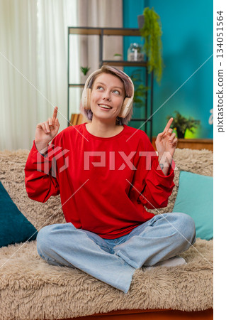 Happy woman dancing happily on sofa listening music in wireless headphones, relaxed joyful emotions Happy woman dancing happily on sofa listening music in wireless headphones, relaxed joyful emotions 134051564
