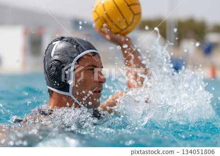 Male water polo player in action, throwing ball in splashing water during competitive match 134051806
