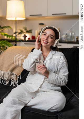 Young woman in wireless headphones enjoys music closes eyes smiles soft head sway calm mood evening 134051952