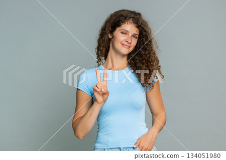 Young happy woman showing peace victory V hand sign cheerful positive joyful optimistic expression Young happy woman showing peace victory V hand sign cheerful positive joyful optimistic expression 134051980