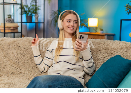 Caucasian woman enjoying relaxing on sofa listening to music with headphones holding smartphone 134052079