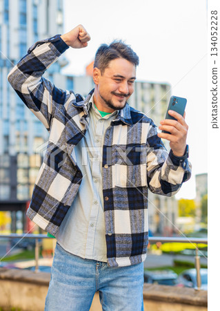 Happy young man using smartphone celebrating victory win good message news on downtown city street 134052228