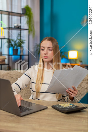 Caucasian woman managing tax declaration at home on sofa table, holding documents, calculator laptop 134052244