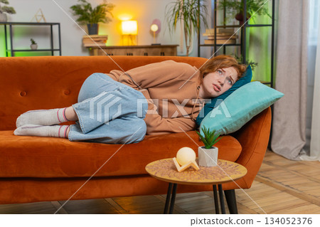 Sick ill redhead woman suffering from period cramps, painful stomach ache on sofa couch at home 134052376