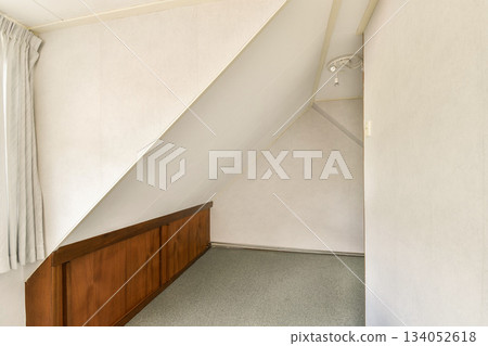 A clean and simple interior corner showcasing neutral tones, a sloping wall, and wooden accents. Ideal for modern home design inspiration and minimalist aesthetics. A clean and simple interior corner showcasing neutral tones, a sloping wall, and wooden accents. Ideal for modern home design inspiration and minimalist aesthetics. 134052618