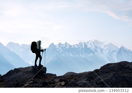 Lone traveler with a backpack standing in front of snow-capped mountains 134053512