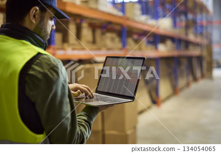 Warehouse worker with laptop auditing stock on shelves, inventory management Warehouse worker with laptop auditing stock on shelves, inventory management 134054065