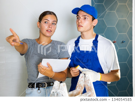 Girl homeowner discussing house renovation work plan with young builder Girl homeowner discussing house renovation work plan with young builder 134054585