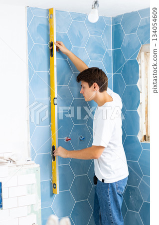 Man using building level on wall in apartment, measuring flatness of wall, working on home improvement Man using building level on wall in apartment, measuring flatness of wall, working on home improvement 134054609