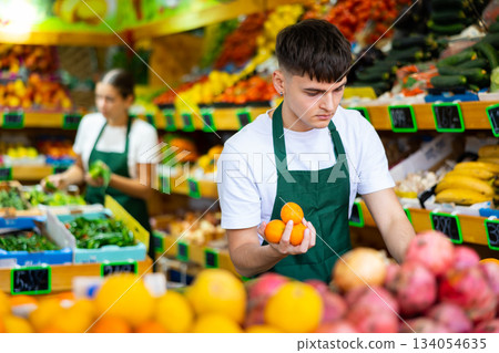 Man store employee displaying assortment of oranges at fruit department in supermarket Man store employee displaying assortment of oranges at fruit department in supermarket 134054635