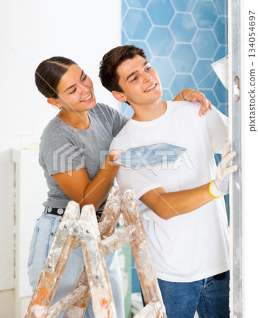 Couple in the bathroom glues ceramic tiles on the wall Couple in the bathroom glues ceramic tiles on the wall 134054697