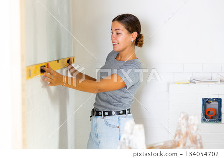 Woman measures deviations from predetermined vertical wall using building level Woman measures deviations from predetermined vertical wall using building level 134054702