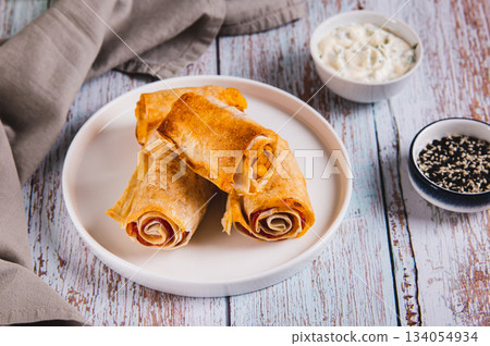Tortilla, ham and cheese in baked rolls on a plate on the table Tortilla, ham and cheese in baked rolls on a plate on the table 134054934