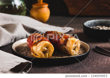 Baked banana roll with bacon on a plate on the table 134054953