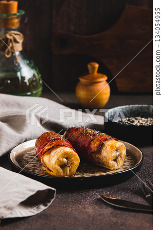 Baked banana roll with bacon on a plate on the table vertical view Baked banana roll with bacon on a plate on the table vertical view 134054955