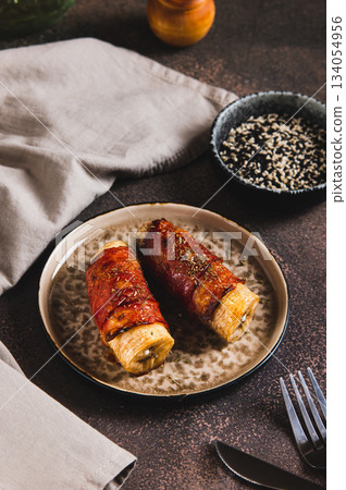 Sweet and Savory Baked Banana Wrapped in Bacon on a Plate on the Table vertical view 134054956