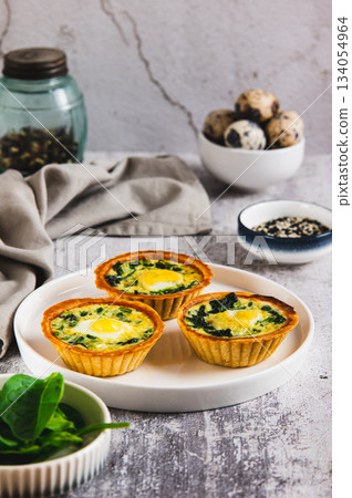 Baked tartlets with quail eggs and fresh spinach on a plate on the table vertical view Baked tartlets with quail eggs and fresh spinach on a plate on the table vertical view 134054964