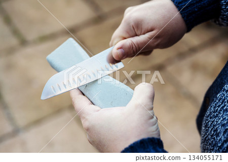 Man 's hand sharpening the kitchen knife with whetstone outdoor 134055171
