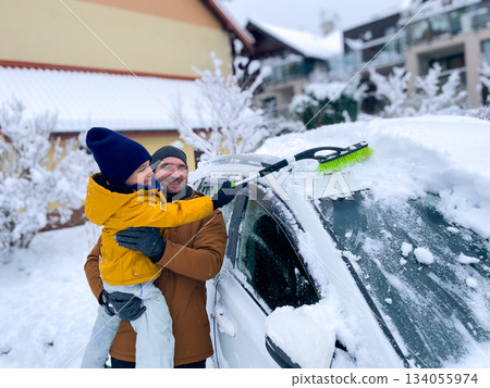 Child and adult clear snow from a parked car in a snowy neighborhood during winter Child and adult clear snow from a parked car in a snowy neighborhood during winter 134055974