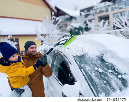 Father and son clear snow from car in snowy neighborhood during winter morning Father and son clear snow from car in snowy neighborhood during winter morning 134055975